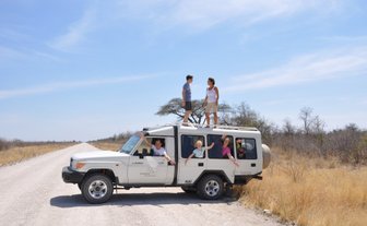 Eine Familie sitzen in einem Jeep. Zwei Personen stehen auf dem Dach des Jeeps - Namibia Familienurlaub