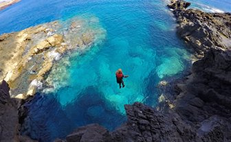 Ein Abenteurer springt von einer Klippe in das glitzernde, türkisfarbene Wasser vor der Küste Madeiras.