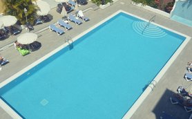 Ein klarer Pool mit sanften Wellen und einer Treppe, umgeben von Liegen und Sonnenschirmen, ideal für Entspannung.
