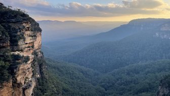 Imposante Klippen erheben sich über eine tiefgrüne, bewaldete Schlucht, während sanfte Nebelschwaden die Landschaft umhüllen.