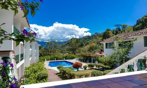 Ein malerischer Blick auf ein Hotel mit einem blauen Pool, umgeben von üppigem Grün und bunten Blumen im Vordergrund.