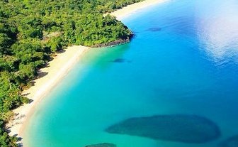 Ein atemberaubender Blick auf einen ruhigen Strand mit klarem, türkisfarbenem Wasser und üppiger grüner Vegetation im Hintergrund.