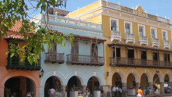 Bunte Kolonialgebäude mit Balkonen und Terrakottadächern, umgeben von grünen Blättern und einem blauen Himmel.