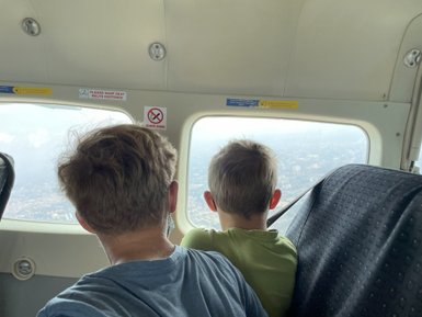 Zwei Kinder sitzen im Flugzeug und schauen aus dem Fenster auf die Stadtlandschaft unter ihnen.