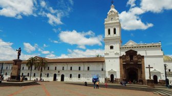 Ein sonniger Platz in Santo Domingo mit einer beeindruckenden Kirche und einer Statue, umgeben von Menschen und Palmen.