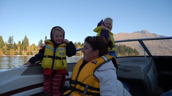 Zwei Kinder in Schwimmwesten lachen fröhlich auf einem Boot, während eine Frau entspannt zuschaut und die Landschaft genießt.