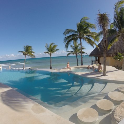 Ein einladender Poolbereich mit Palmen, wo Familienmitglieder entspannt im Wasser spielen und die Sonne genießen.