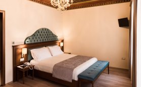 Ein elegantes Hotelzimmer mit einem großen, gepolsterten Bett und einem blauen Hocker am Fußende, umgeben von sanften Farben.
