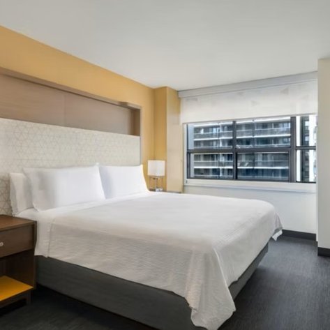 Ein modernes Hotelzimmer mit einem großen Bett, hellen Wänden und einem Fenster, das auf die Stadt blickt.