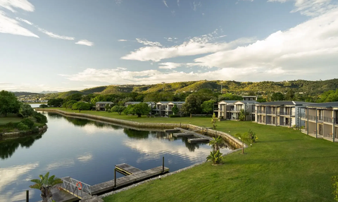 Eine ruhige Landschaft mit einem klaren Wasserlauf, umgeben von üppigem Grün und modernen Gebäuden im Hintergrund.