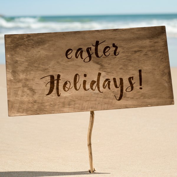 Ein Holzschild steht am Strand und verkündet fröhlich die Osterferien mit geschwungener Schrift.