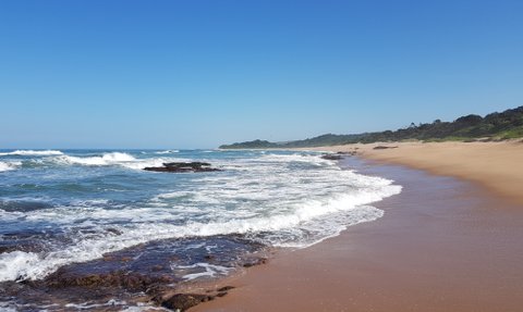 Ein ruhiger Strand mit sanften Wellen, die auf den goldenen Sand treffen, unter einem strahlend blauen Himmel.