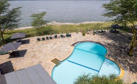 Ein einladender Pool mit blauen Wasser und einer Steinoberfläche, umgeben von Liegen und Sonnenschirmen am Ufer eines Sees.