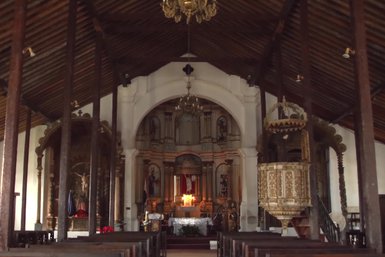 Die Innenansicht einer historischen Kirche mit einem kunstvoll gestalteten Altar und Holzdecke, die eine ruhige Atmosphäre schafft.