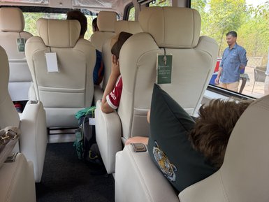 Im Inneren eines komfortablen Busses sitzen mehrere Personen, während ein Fahrer draußen steht und mit jemandem spricht.