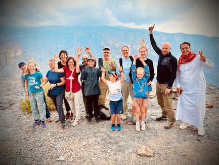 Reisegruppe posiert gemeinsam mit ihrem Guide vor der Bergkulisse des Jebel Shams – Oman Reise mit Kindern