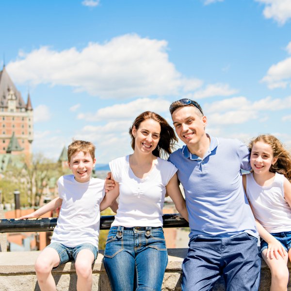 Eine glückliche Familie posiert vor dem beeindruckenden Château Frontenac, umgeben von strahlend blauem Himmel und Wolken.