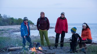 Eine Familie steht um ein Lagerfeuer, während die Kinder Marshmallows grillen