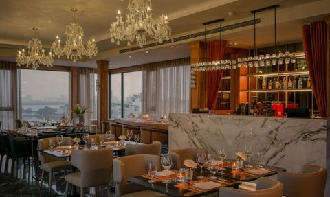 Elegante Restaurant mit stilvollen Möbeln, Kronleuchtern und einem Blick auf die Stadt durch große Fenster.