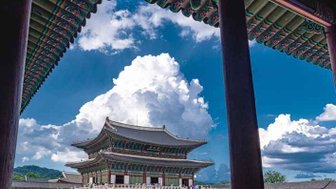 Der Blick durch die Säulen zeigt das beeindruckende Gyeongbokgung-Palastgebäude unter einem strahlend blauen Himmel.