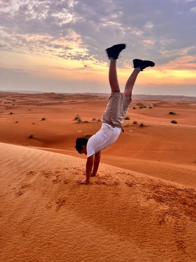 Junge macht Handstand in der Wahiba-Wüste beim Sonnenuntergang – Oman Reise mit Kindern