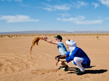Guide und Kind spielen gemeinsam und werfen Sand in der weiten Wüste – Familienreise nach Marokko