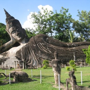 Eine massive, liegende Buddha-Statue dominiert den Park, umgeben von üppigem Grün und weiteren kleineren Statuen.