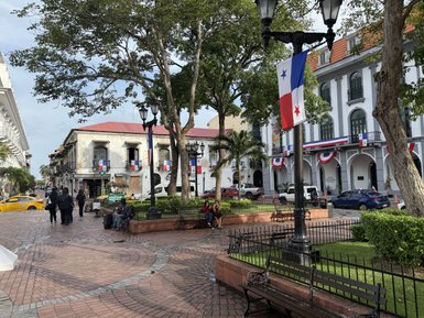 Eine belebte Straße in Panama City mit historischen Gebäuden und bunten Flaggen, die eine festliche Atmosphäre schaffen.
