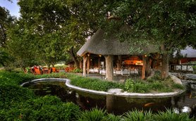 Ein einladendes Restaurant mit Strohdach, umgeben von üppigem Grün und einem ruhigen Teich, der die Natur widerspiegelt.