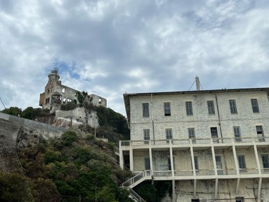 Die verfallene Alcatraz-Anlage erhebt sich majestätisch über die grüne Küstenlandschaft unter einem bewölkten Himmel.