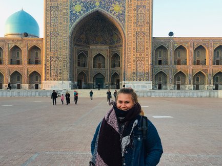 Eine Frau steht lächelnd vor der beeindruckenden Architektur des Registan in Samarkand, umgeben von Besuchern.