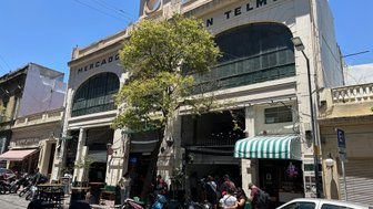 Der Mercado de San Telmo in Buenos Aires zeigt eine lebendige Straßenszene mit Menschen und Motorrädern vor dem Gebäude.