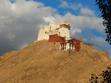 Ein majestätisches Kloster thront auf einem steilen Hügel, umgeben von dramatischen Wolken und goldenem Licht.