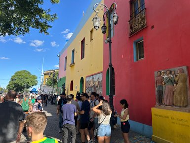 Bunte Gebäude in Buenos Aires umgeben von Menschen, die an einer belebten Straße stehen und miteinander sprechen.