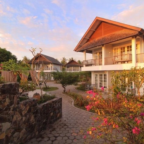 Ein charmantes Resortgebäude mit zwei Etagen, umgeben von üppigem Grün und bunten Blumen im warmen Abendlicht.