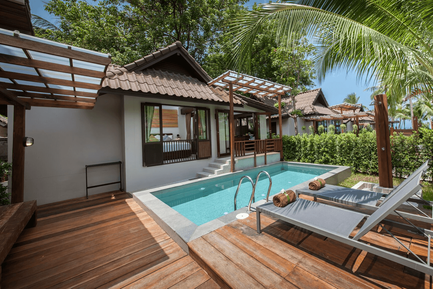 Ein einladender Poolbereich mit Liegen und Handtüchern, umgeben von üppigem Grün und modernen Bungalows im Hintergrund.