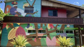 Bunt bemalte Fassade eines Gebäudes mit dem Schriftzug 'El Sendero del Cacao' und tropischen Pflanzen im Vordergrund.
