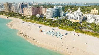 Ein atemberaubender Blick auf den Strand von Miami Beach, umgeben von modernen Hotels und Palmen unter klarem Himmel.