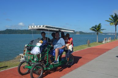 Eine Gruppe von fünf Personen sitzt in einem grünen Fahrrad-Rikschawagen am Amador Causeway in Panama City.