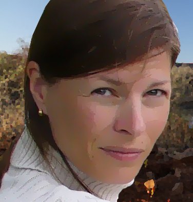 Eine Frau mit braunen Haaren und einem weißen Pullover schaut direkt in die Kamera, mit einem ernsten, nachdenklichen Ausdruck.