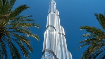 Der Burj Khalifa erhebt sich majestätisch gegen den klaren blauen Himmel, umgeben von üppigen Palmen.