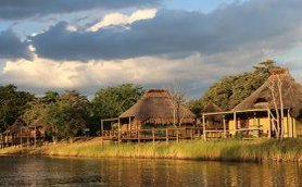 Eine friedliche Landschaft mit traditionellen Hütten am Ufer eines ruhigen Gewässers, umgeben von üppigem Grün.