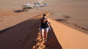 Eine Mutter läuft mit Ihrem Kind auf dem Rücken eine Düne hinauf - Namibia Reise mit Kindern