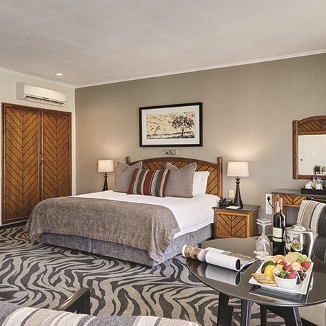 Ein elegantes Hotelzimmer mit einem großen Bett, stilvollen Möbeln und einem kleinen Tisch mit frischem Obst und Wein.