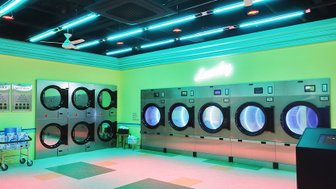Ein moderner Waschsalon mit leuchtend grünen Wänden und bunten Neonlichtern, die eine einladende Atmosphäre schaffen.
