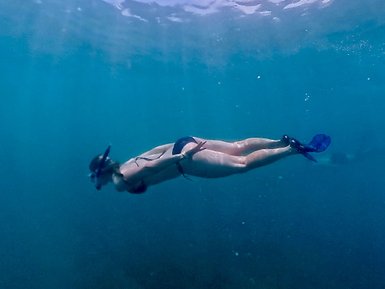 Eine Person taucht elegant unter Wasser und erkundet die ruhigen, blauen Tiefen des Ozeans mit einer Schnorchelausrüstung.