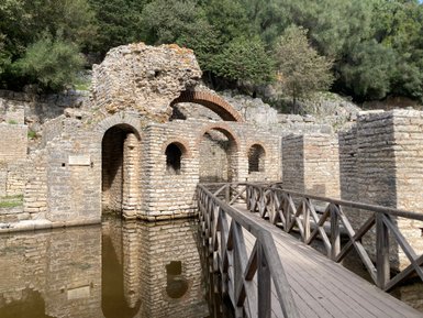 Die Überreste einer alten Steinstruktur spiegeln sich im ruhigen Wasser, umgeben von üppigem Grün und Felsen.