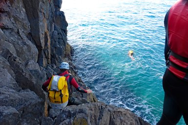 Ein Abenteurer in einem Neoprenanzug balanciert auf den Felsen, während ein anderer im klaren Wasser schwimmt.