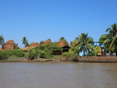 Eine ruhige Flusslandschaft mit üppigem Grün und traditionellen roten Ziegeldächern unter einem strahlend blauen Himmel.