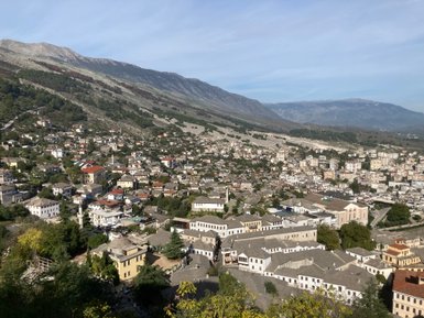 Ein weitläufiger Blick auf die Stadt Gjirokaster, umgeben von sanften Hügeln und majestätischen Bergen im Hintergrund.
